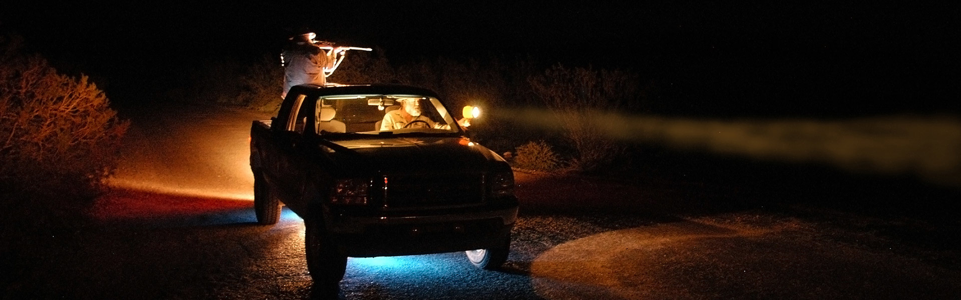 FWP wardens in a truck using lights to look out into a field at night.