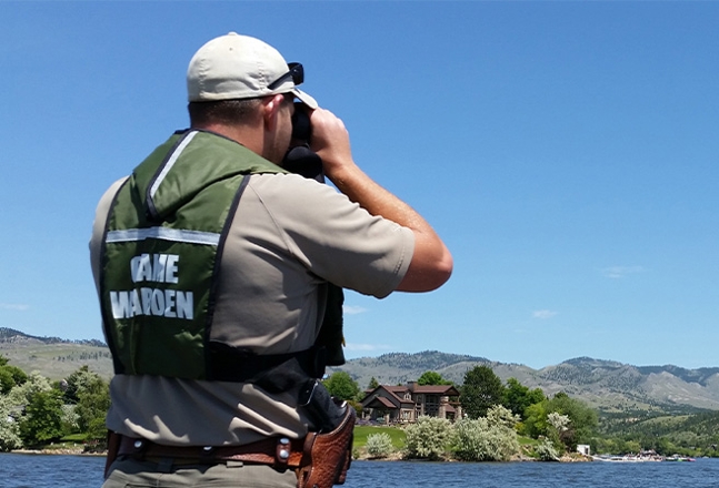 An FWP Warden using binoculars on the water